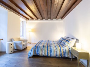 Un dormitorio con cama, una silla, una mesita de noche y una lámpara.