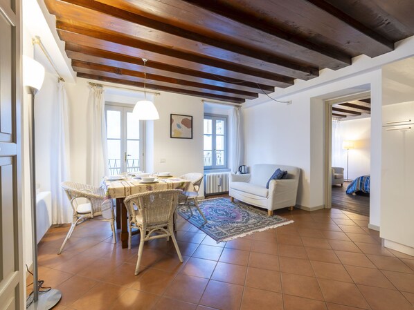 Un amplio espacio de sala con una mesa de comedor, sillas de mimbre, un sofá blanco y un tapete estampado.