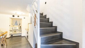 Un intérieur moderne avec un escalier menant à un deuxième étage, un coin cuisine équipé d’appareils électroménagers et un espace repas avec des chaises.