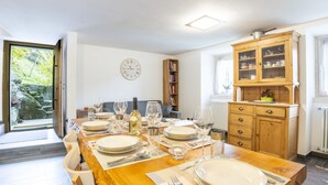 Un coin repas avec une table en bois dressée pour quatre personnes, une horloge au mur et une vue sur l’extérieur.