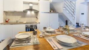 Une cuisine moderne dotée d’une cuisinière encastrée et d’une hotte en acier inoxydable. On y trouve également un coin repas avec une table en bois, dressée pour quatre personnes, et agrémentée d’assiettes, de verres et de couverts.
