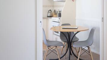 A small dining area with a round table and four chairs, a kitchen in the background with a stove and utensils, and a fire extinguisher on the wall.