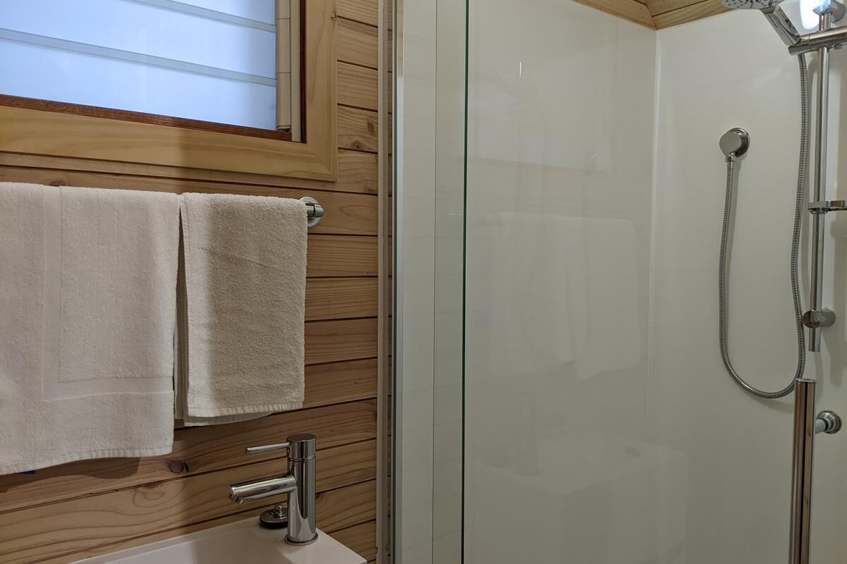 A bathroom with a glass shower enclosure, wooden panel walls, and a sink with a faucet.