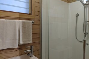 A bathroom with a glass shower enclosure, wooden panel walls, and a sink with a faucet.