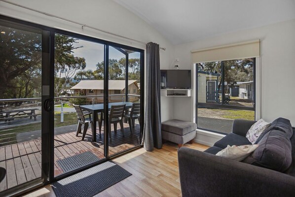 A modern living room with a sliding glass door leading to an outdoor deck, a sofa, a TV mounted on the wall, and a small table.