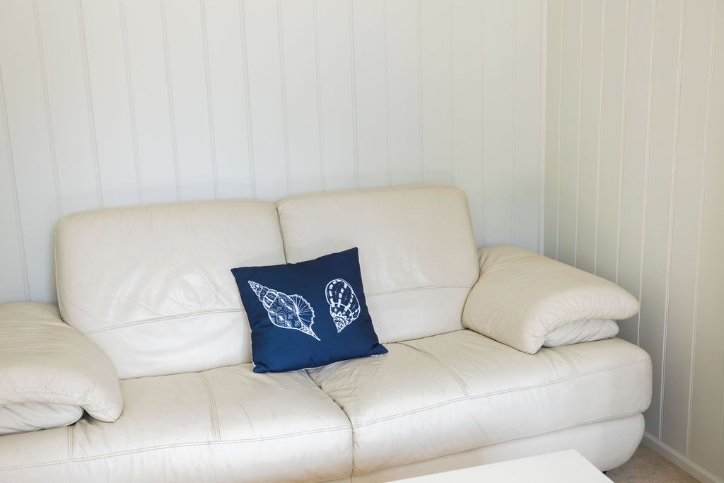 A beige leather sofa with a dark blue pillow featuring a leaf pattern, positioned against a light-colored wall with vertical stripes.