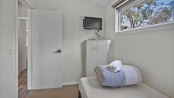 Una habitación pequeña y limpia con una cama, un televisor montado en la pared y una ventana con vistas a árboles.