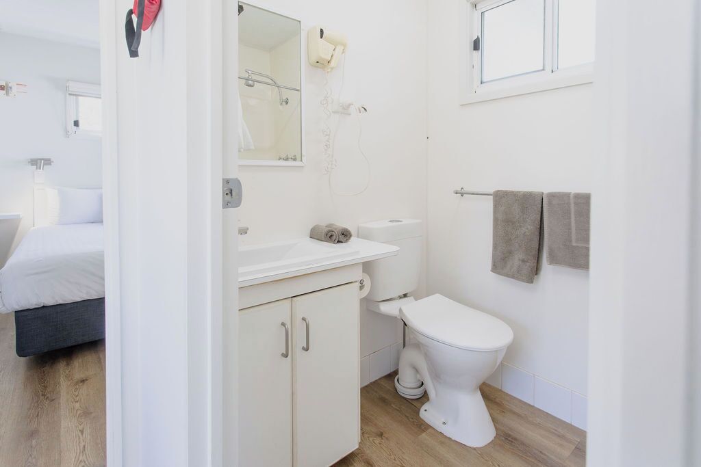 Ein modernes Badezimmer mit Toilette, Waschbecken und Spiegel. Im angrenzenden Raum ist ein Bett zu sehen.