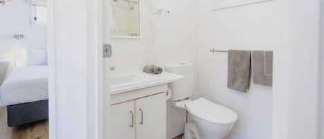 Une salle de bain moderne avec des toilettes, un lavabo et un miroir. On peut apercevoir un lit dans la pièce adjacente.