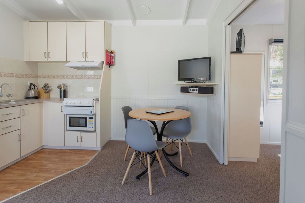 A compact kitchen with a microwave, kettle, and a small dining table with chairs.