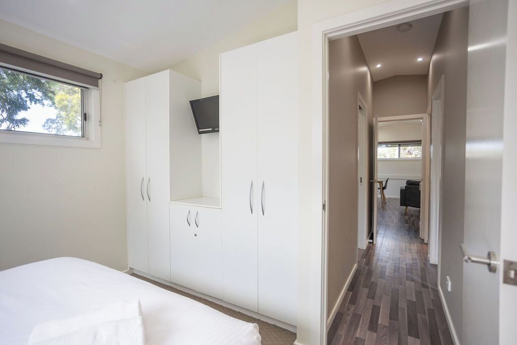 A bedroom with a bed, white wardrobe, and a TV mounted on the wall.