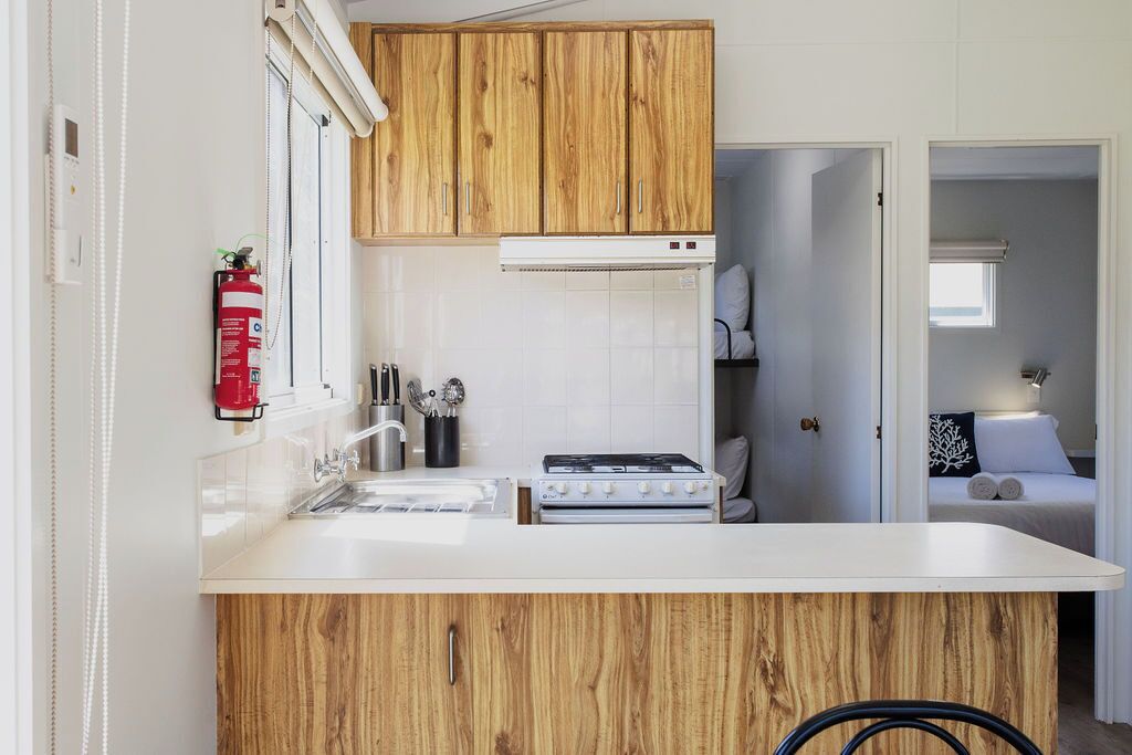 A compact kitchen with wooden cabinets, a white countertop, a gas stove, and a built-in oven.