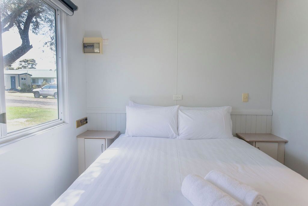 Una habitación de hotel con una cama grande, dos mesitas de noche, un ventanal y un termostato en la pared.