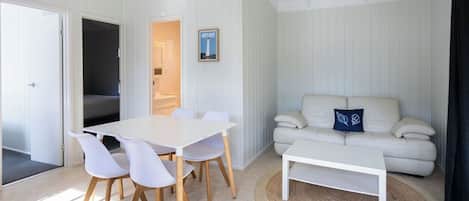 Een moderne woonkamer met een witte bank, een witte salontafel en een eethoek met een witte tafel en stoelen.