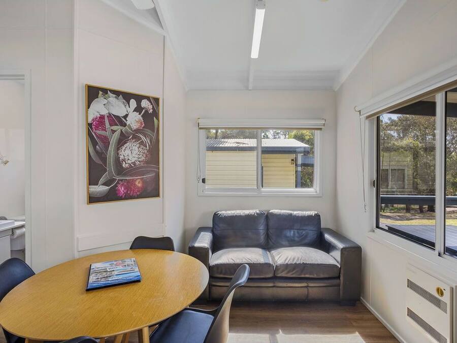 A modern living room with a wooden dining table, a leather sofa, and a large window providing a view of the outdoors.