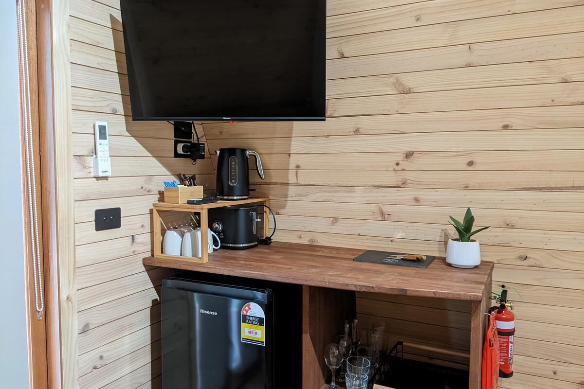 A compact kitchenette with a black refrigerator, a coffee maker, and a flat-screen TV mounted on a wooden wall.