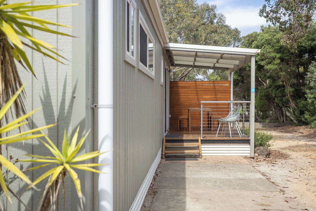 Uma casa moderna com varanda coberta, deck de madeira e caminho de concreto.