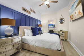 Une chambre à coucher comprenant un lit, des tables de chevet, un ventilateur de plafond, un téléviseur et une boussole fixée au mur.