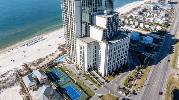 Un hôtel de grande hauteur, avec de nombreux étages, une vue sur la plage et un court de tennis.
