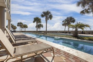 Un espace piscine agrémenté de chaises longues, de palmiers et d’un ciel dégagé.