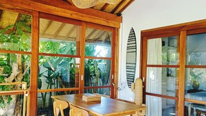 Un coin repas en bois, avec un mur en verre et une planche de surf accrochée au mur.