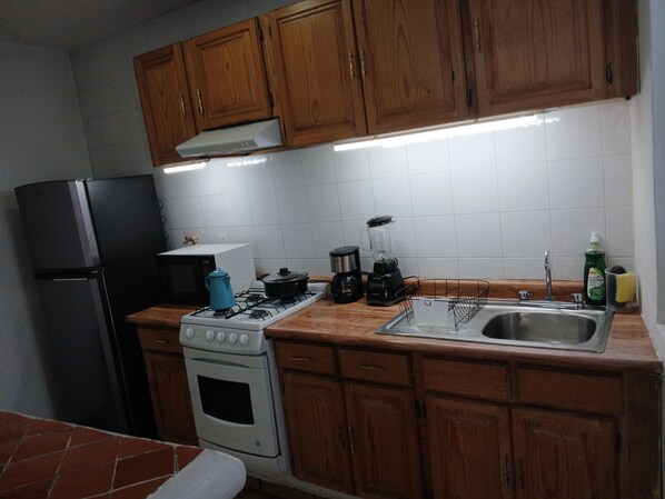 A kitchen with wooden cabinets, a stove, a refrigerator, a microwave, a coffee maker, and a sink.