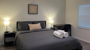 A bedroom with a bed, two bedside lamps, a desk, and a window with blinds.