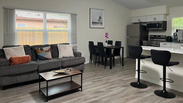 A modern living room with a grey sofa, a coffee table, and a dining area with a table and chairs.