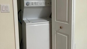 A compact laundry room with a stacked washer and dryer, a door with a round handle, and a light switch on the wall.