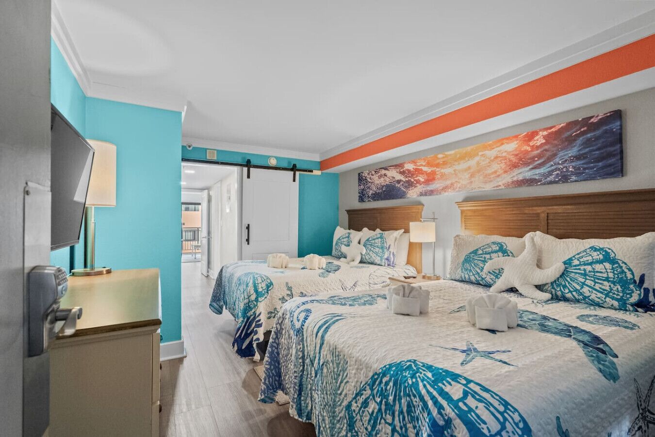 A hotel room with two beds, a TV, a desk, and a large painting on the wall.