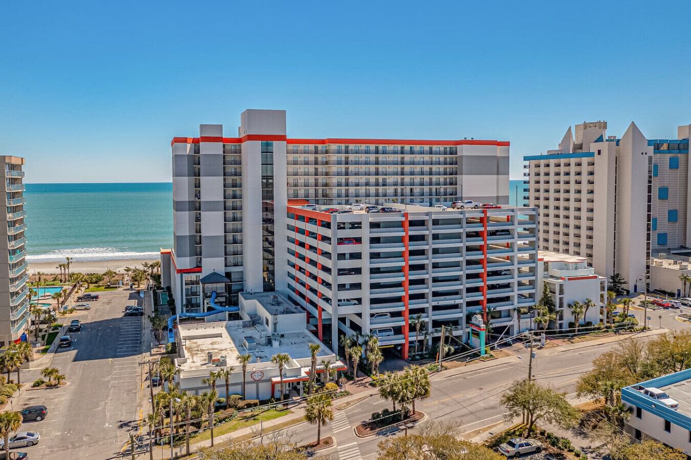 Een meerlaags hotel met een parkeergarage, nabij een strand en uitzicht op de oceaan.
