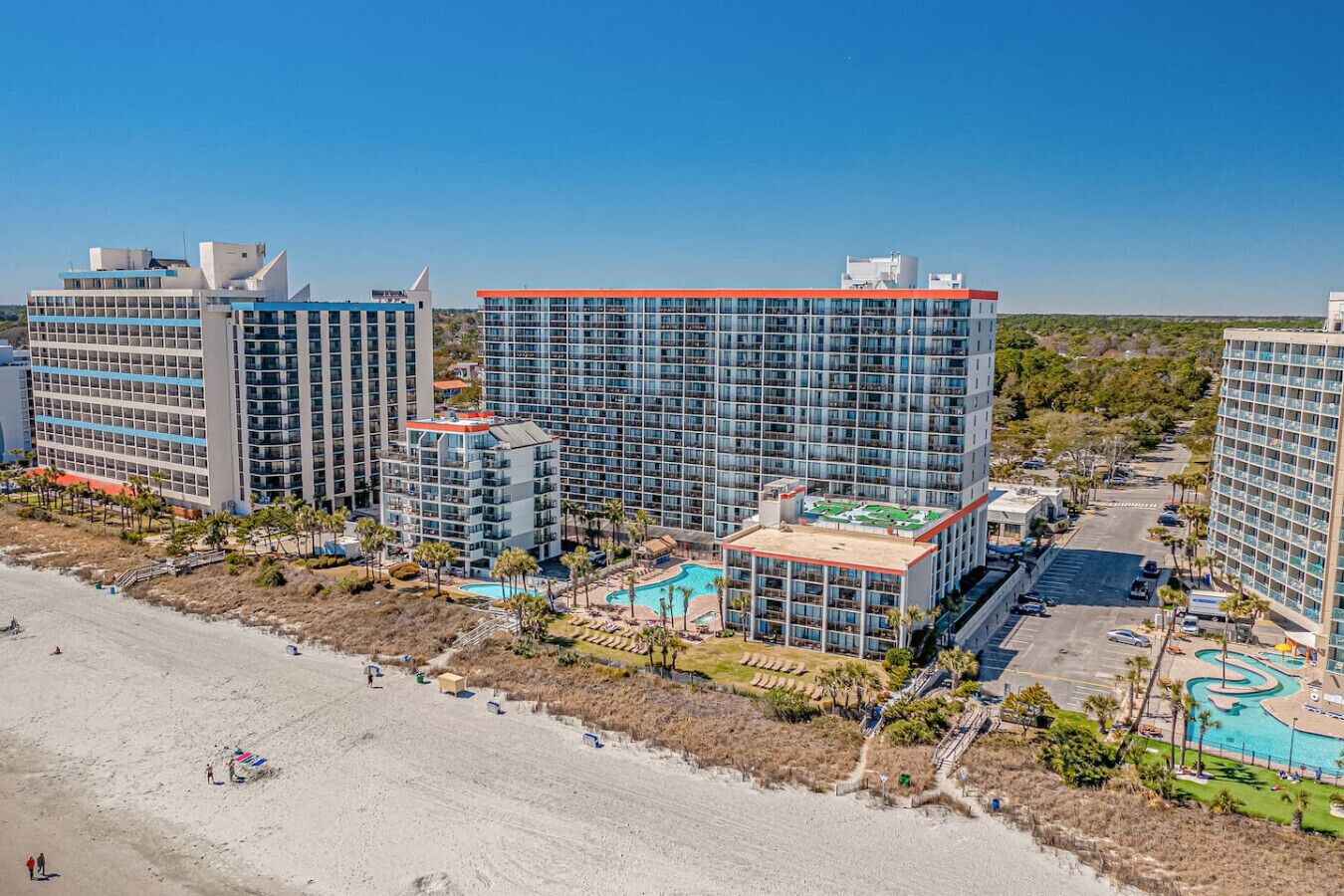A high-rise hotel complex with multiple buildings, a swimming pool, and a beach area.