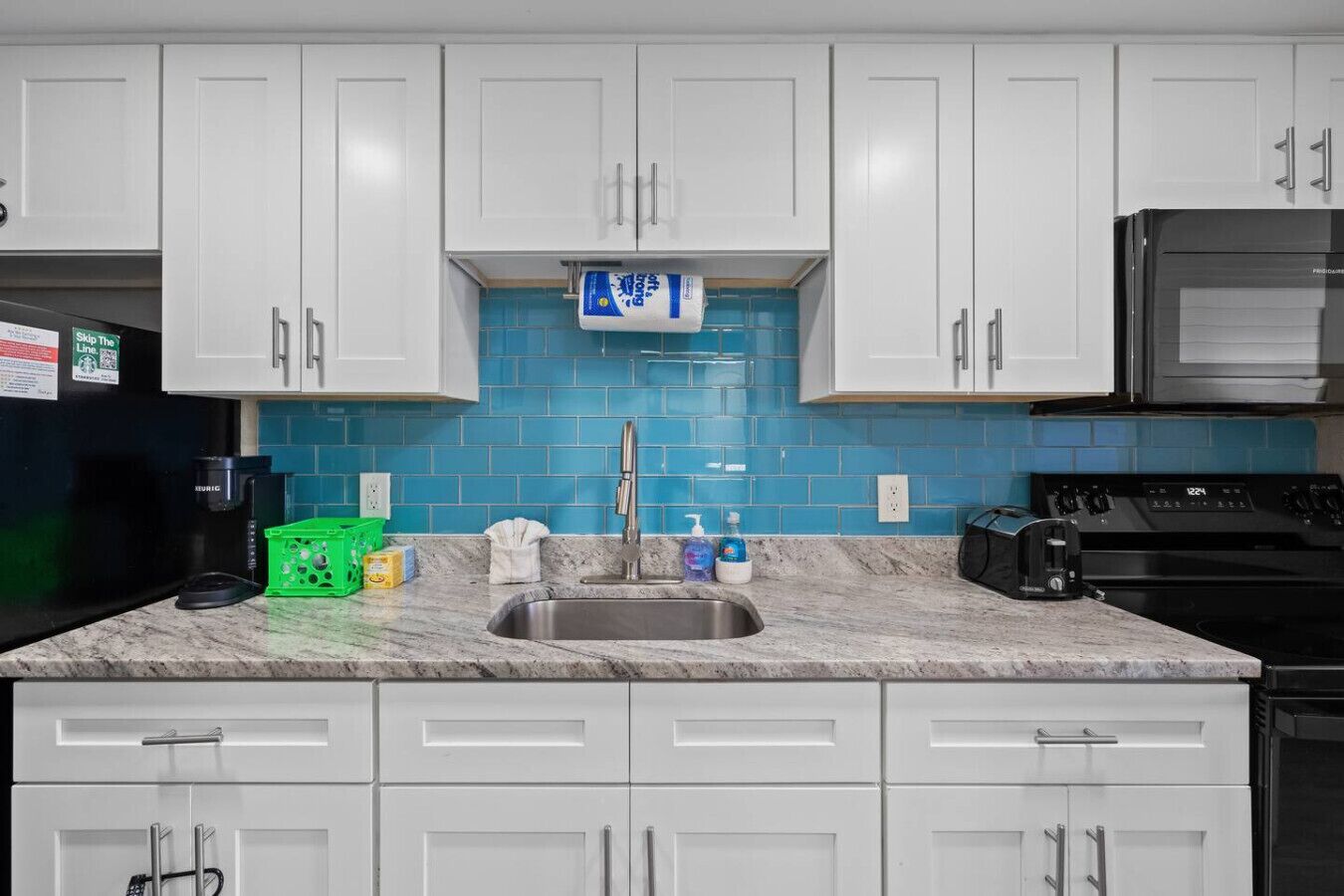 A kitchen with white cabinets, a blue tiled backsplash, a stainless steel sink, and a black stove.