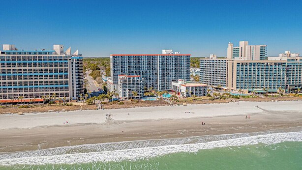 Een hotel aan het strand met meerdere hoge gebouwen, een zandstrand en een helderblauwe lucht.