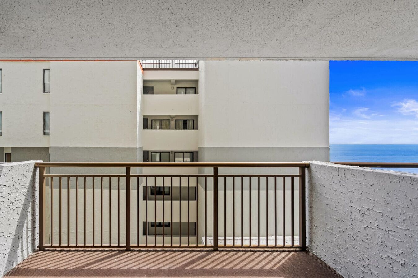 Uma varanda com guarda-corpo de metal, vista de um edifício com vários andares e um céu azul límpido.