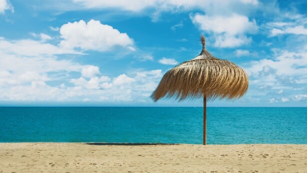 A beach with a thatched umbrella and a clear blue sky.