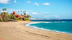 A beach with a building featuring palm trees and a clear view of the ocean.