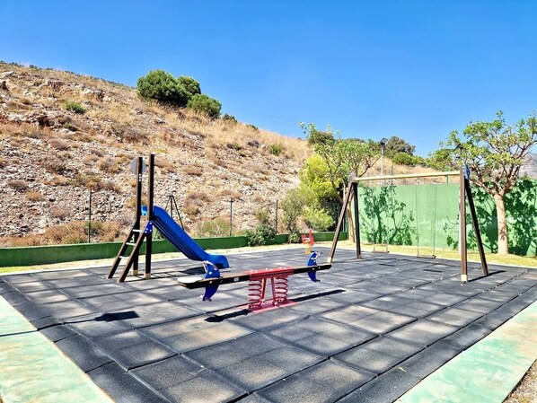 Un parque infantil con un tobogán azul, columpios y un balancín.