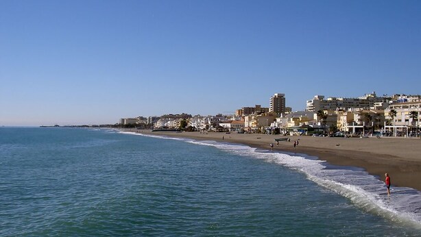 A coastal cityscape with a beach, buildings, and a clear sky.