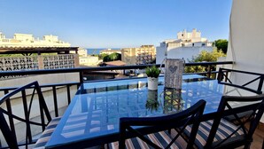 A glass-top table with striped cushions on a balcony overlooking a cityscape.
