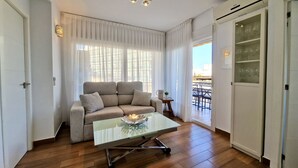 A modern living room with a sofa, a glass coffee table, and a view of the outside balcony.