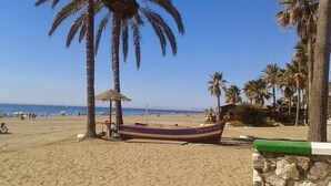 A beach with a boat, palm trees, and a clear sky. - SR Wellingtonia Estepona Downtown (Estepona)
