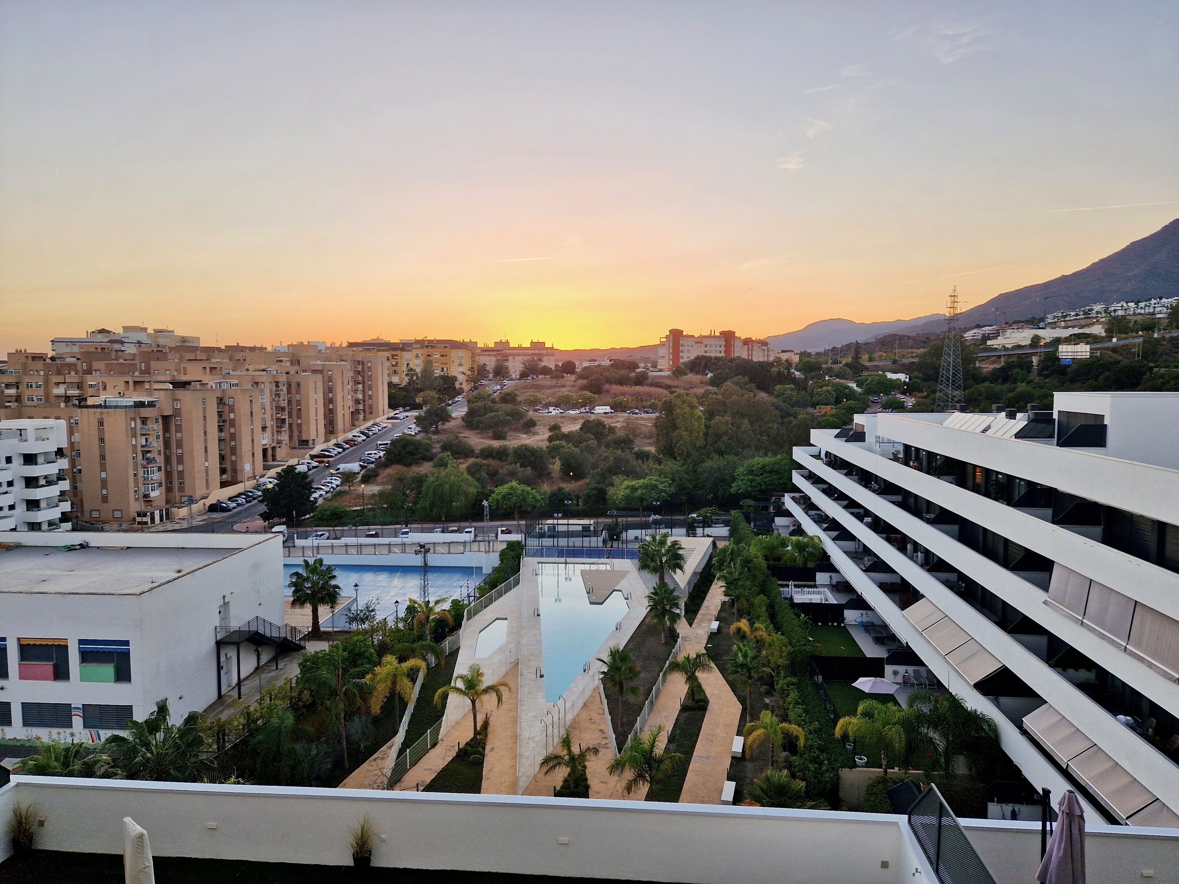 Ein modernes Gebäude mit Pool auf dem Dach und Blick auf eine Stadtlandschaft bei Sonnenuntergang.