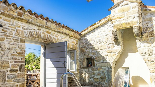 Un edificio de piedra con piscina, una puerta y un ventanal pequeño.