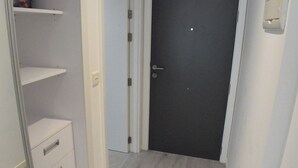 A narrow hallway with a door at the end, a white shelf unit with drawers, and a light-colored wooden floor. - Luxury Studio in Gibraltar (Gibraltar)