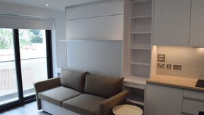 A modern living room with a sofa, a small table, built-in shelving, and a sliding door leading to a balcony. - Luxury Studio in Gibraltar (Gibraltar)