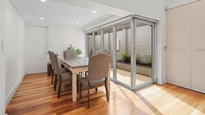 Comedor con mesa y sillas de madera, puerta corrediza de vidrio que da a un balcón con plantas.
