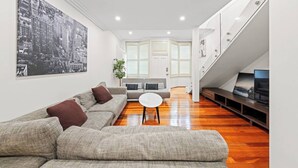 Una sala de estar moderna con un sofá modular, una mesa de centro redonda y una escalera que lleva a un nivel superior.