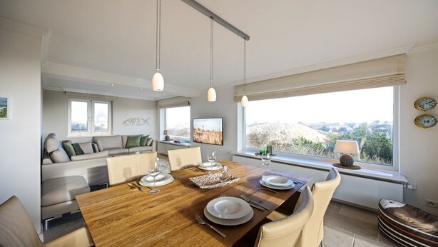 Un comedor moderno con una mesa de madera dispuesta para cuatro personas, un sofá y un amplio ventanal con vistas.