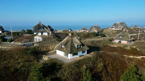 Un pueblo costero con casas de techos de paja tradicionales, algunas con ampliaciones modernas, rodeado de vegetación natural y una vista despejada del mar.